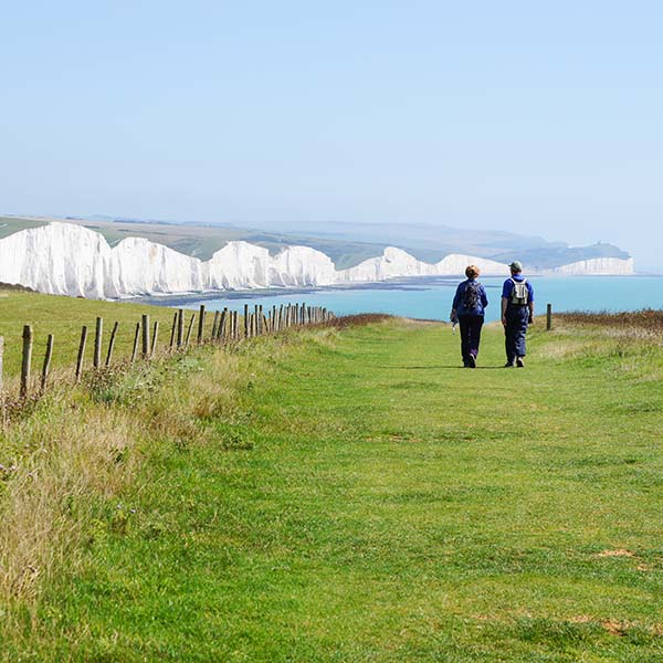 Walkers striding towards the Seven Sisters chalk cliffs in East Sussex England